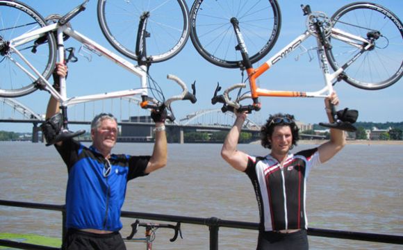 two cyclists holding their bicycles above their heads on the riverfront in downtown davenport iowa