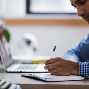 picture of man taking notes in front of laptop